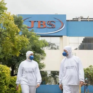Frente da fábrica da JBS (JBSS3) com dois funcionários com roupas brancas para manuseio de carnes