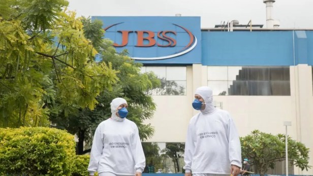 Frente da fábrica da JBS (JBSS3) com dois funcionários com roupas brancas para manuseio de carnes