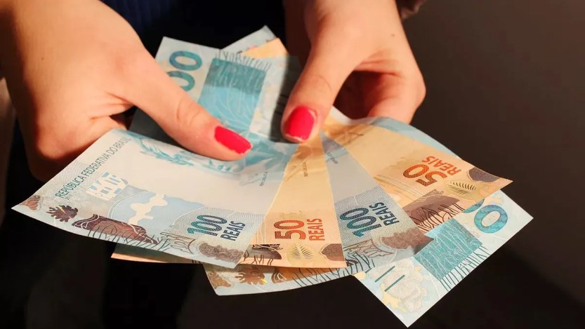 Foto de duas mãos segurando notas de 50 reais e 100 reais para a matéria sobre mitos do mercado financeiro.