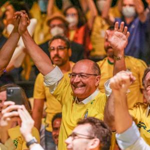 Foto de Geraldo Alckmin e de Gleisi Hoffman vestindo a camisa da seleção brasileira e comemorando um gol