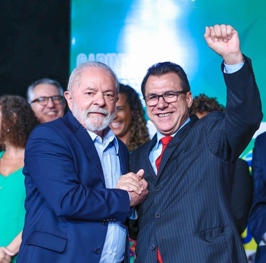 Foto de Lula à direita, de palitó azul, cumprimentando Luiz Marinho, ministro do Trabalho, à esquerda