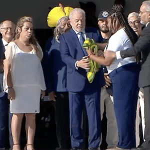 Sem a presença do ex-presidente Jair Bolsonaro, Lula recebe, emocionado, a faixa presidencial das mãos de representantes do povo brasileiro. (Foto: TV Globo/Reprodução)