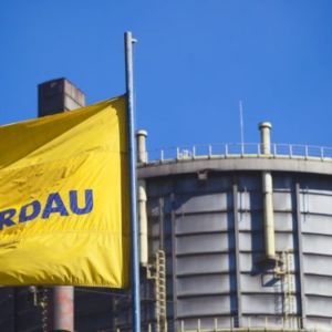 Foto de uma planta da Gerdau (GGBR4) com uma bandeira de fundo amarelo com logo azul da empresa.
