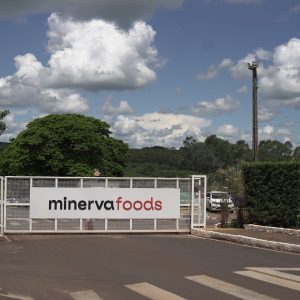 Foto de portão de planta industrial da Minerva Foods (BEEf3) em Barretos. O portão tem o logo da companhia.