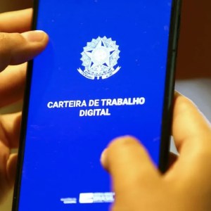 Foto de um celular com a tela azul da carteira de trabalho digital. Duas mãos seguram o aparelho.