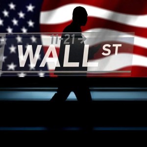Foto de uma placa com os dizeres "Wall Street ST", com um homem andando ao fundo e uma imagem da bandeira dos Estados Unidos