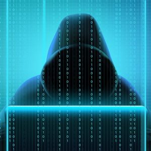 Imagem de um homem encapuzado com o rosto coberto na frente de um computador, hacker