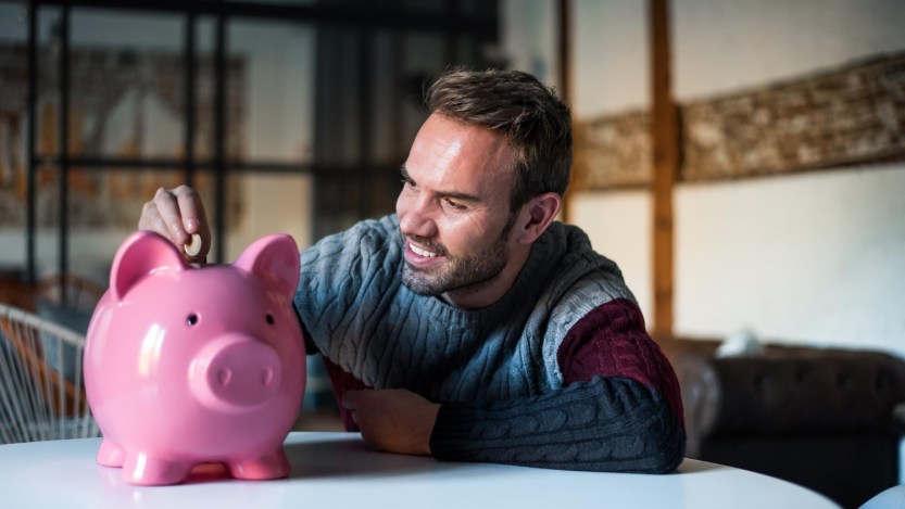 Imagem para o texto sobre quanto rendem R$ 200 mil na poupança em que está um homem colocando moedas em um cofrinho de porco cor de rosa.