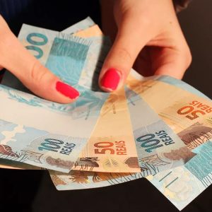 Mãos femininas seguram notas de real brasileiro de 100 e 50 reais
