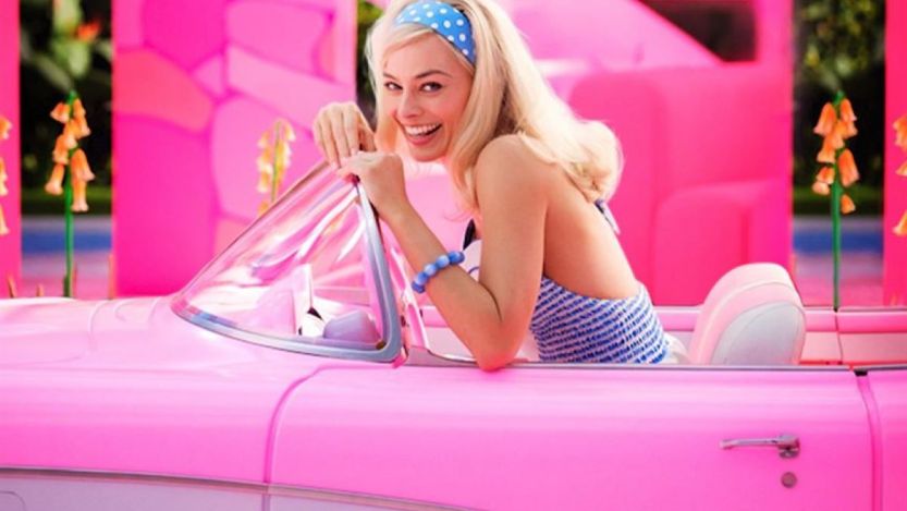 Margot Robbie, que interpreta Barbie no filme, sentada em um carro rosa em cena