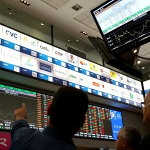 Foto da bolsa de valores brasileira, a B3. Na imagem, um analista aponta para o painel enquanto outros observam. A matéria é sobre abertura do mercado