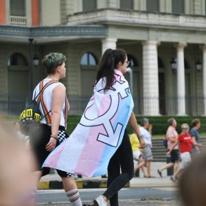 Jovens caminham usando símbolos LGBTQIA+ e bandeira do movimento trans