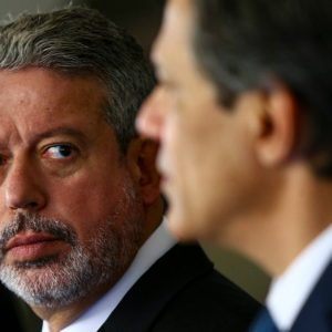 Foto de Arthur Lira olhando para o ministro Fernando Haddad com expressão de foco. A matéria descreve os desafios para a aprovação da meta fiscal nesta semana.
