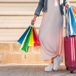 Mulher com mala de viagem e sacolas de compras simbolizando como fazer o dinheiro render para uma viagem