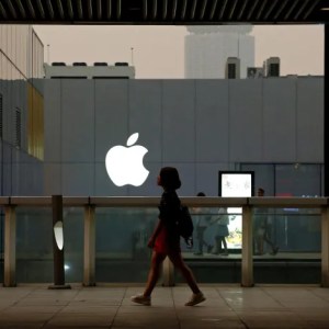 Foto mostra mulher caminhando me frente a prédio com o logo da Apple