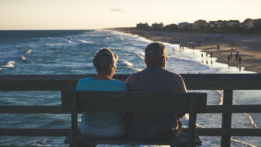 Imagem de duas pessoas sentadas olhando o mar para a matéria sobre como juntar dinheiro para uma aposentadoria de R$ 3 mil.
