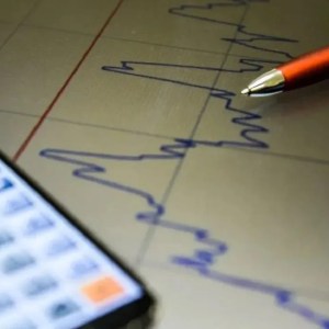 Foto de uma caneta e um celular com calculadora sobre um gráfico; a matéria descreve a queda no rendimento do Tesouro IPCA+ em agosto