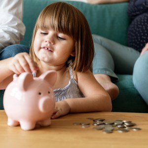 Foto de uma menina colocando moedas em um porquinho para a matéria sobre investimento para filhos