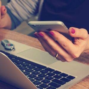 Imagem para o texto sobre segurança em pagamento online em que aparece uma mão segurando um celular em frente a um notebook.