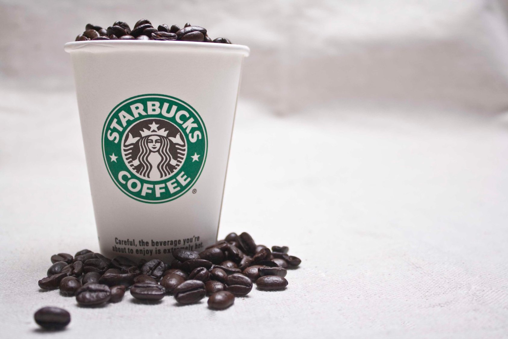 Foto de um copo da rede Starbucks com grãos de café em cima.