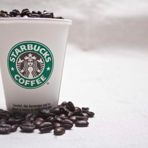 Foto de um copo da rede Starbucks com grãos de café em cima.
