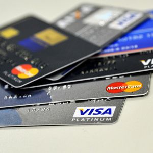 Cartões de crédito de cores cinza, preto e azul sobrepostos sobre mesa.