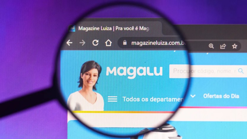 Foto de uma lupa sobre o logo e o mascote virtual da Magazine Luiza (MGLU3). a Matéria fala sobre as melhores ações da bolsa de valores nesta quinta-feira (23)
