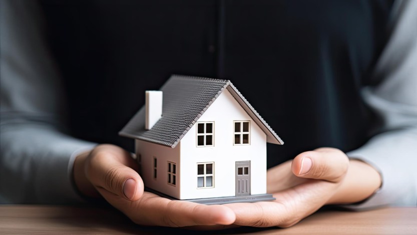 Imagem de uma mão segurando uma maquete de uma casa para a matéria sobre quitar o financiamento ou investir.