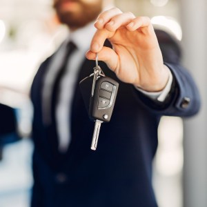 Imagem para o texto sobre como comprar o primeiro carro e como comprar uma casa em que aparece um homem de terno segurando uma chave de um automóvel.
