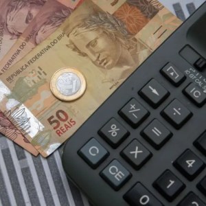 Imagem para a matéria sobre como não se endividar em qua aprecem notas de 50 reais e 10 reais e uma moeda de 1 real com uma calculadora ao lado.