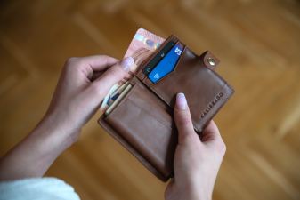 Imagem para o texto sobre dismorfia financeira em que aparece uma mão segurando uma carteira aberta e retirando uma nota de dentro.