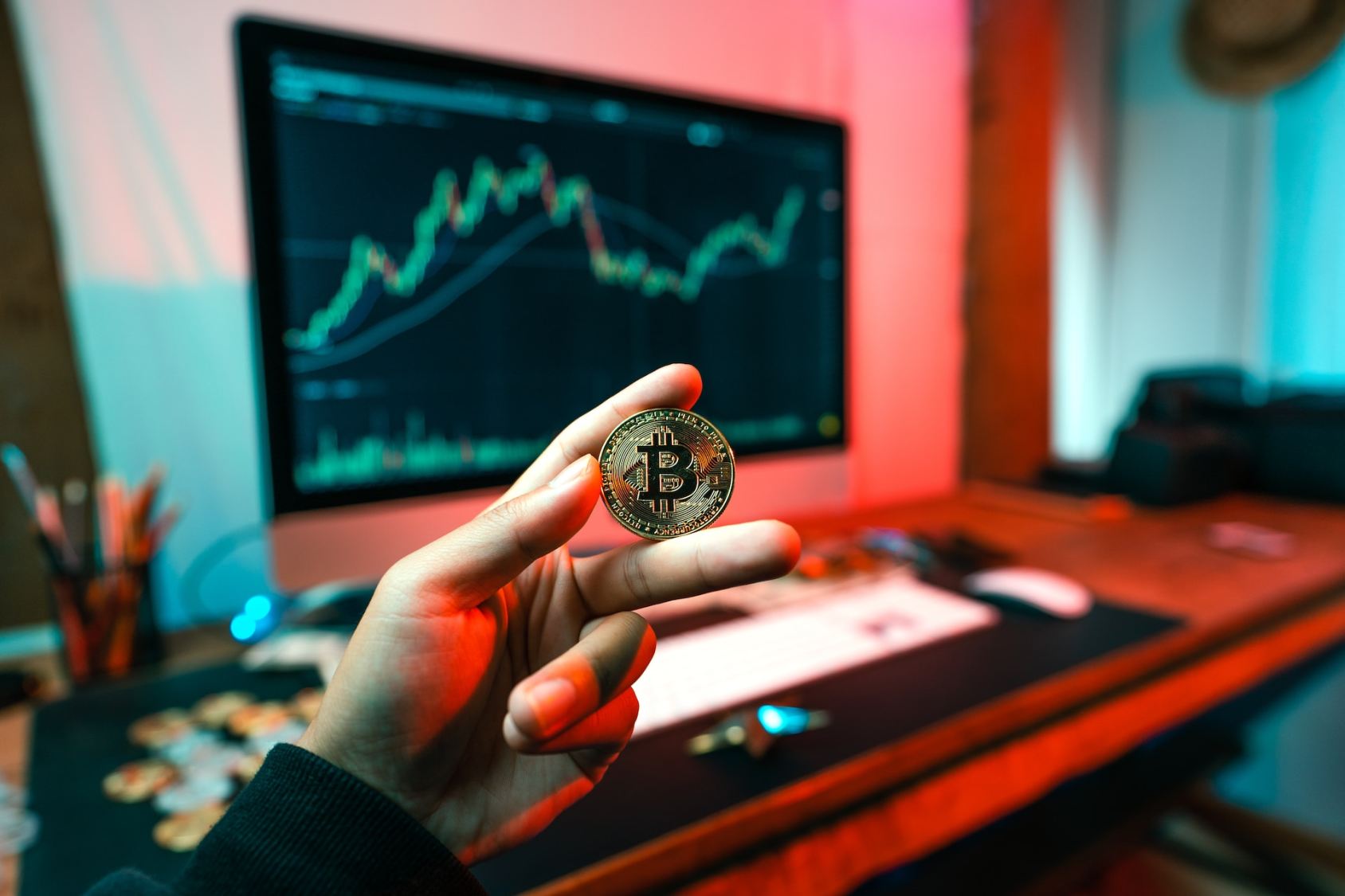 Imagem para a matéria sobre futuro das criptomoedas em que uma mão segura uma moeda de bitcoin com uma computador ao fundo.