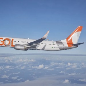 Foto de um avião da Gol com a cauda laranja e o logo da empresa. A matéria descreve a queda das ações da Gol (GOLL4) no Ibovespa.