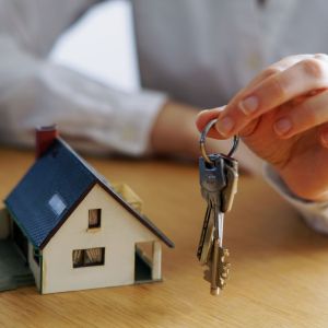 Pessoa com uma chave na mão e uma maquete de uma casa