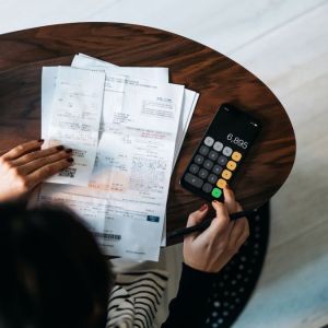 Imagem para a matéria sobre dicas para economizar dinheiro em que aparece uma mulher fazendo cálculos e olhando boletos.