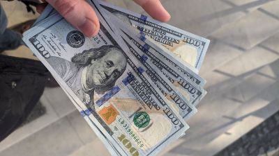 Imagem para a matéria sobre investimento no exterior em que aparece uma mão segurando seis notas de 100 dólares.