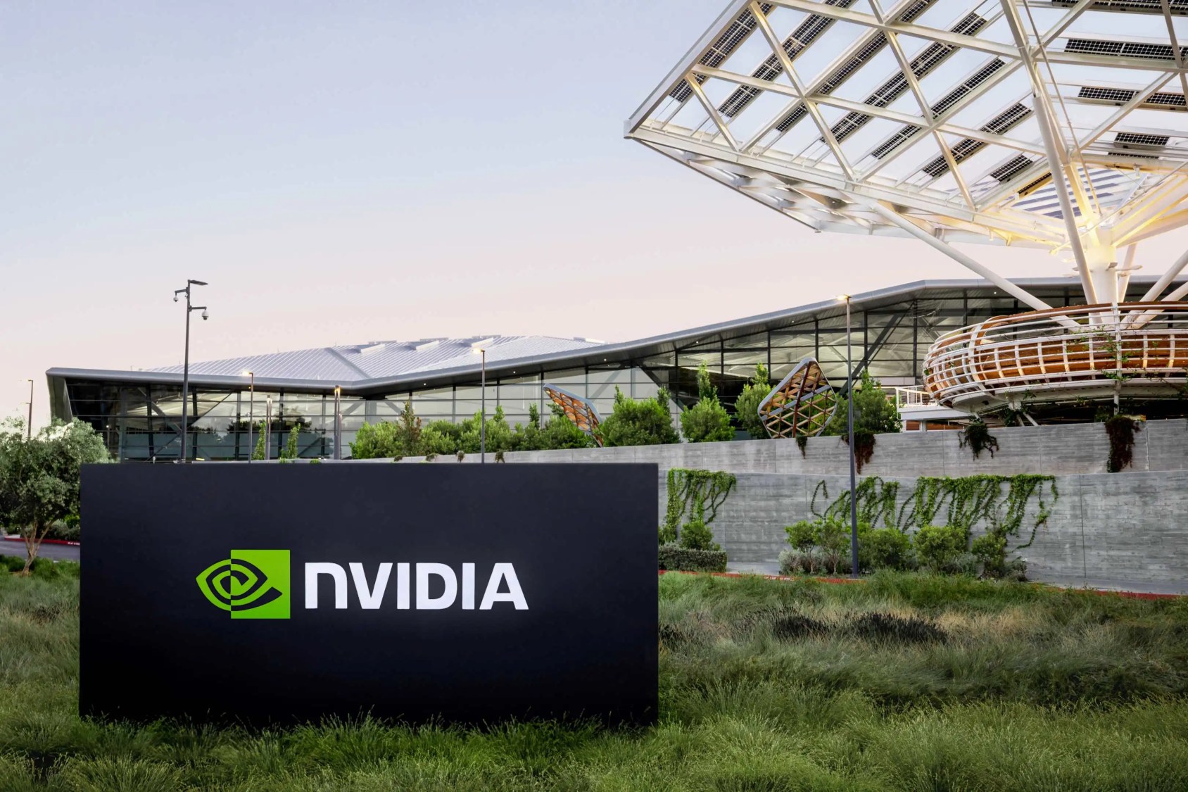 Imagem de uma placa preta em um gramado com o escrito "Nvidia". Atrás, a sede de uma empresa de tecnologia.