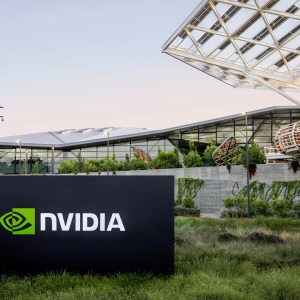 Imagem de uma placa preta em um gramado com o escrito "Nvidia". Atrás, a sede de uma empresa de tecnologia.