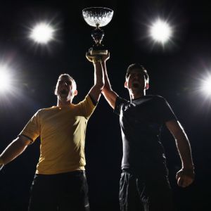 Imagem para o texto sobre os prêmios do futebol em que aparecem dois jogadores homens segurando uma taça
