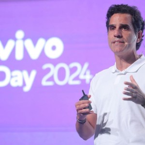 Foto de Christian Gebara, CEO da Telefônica Brasil (VIVT3). Ele é branco, usa camisa branca e fala a um microfone com um painel da Vivo ao fundo.