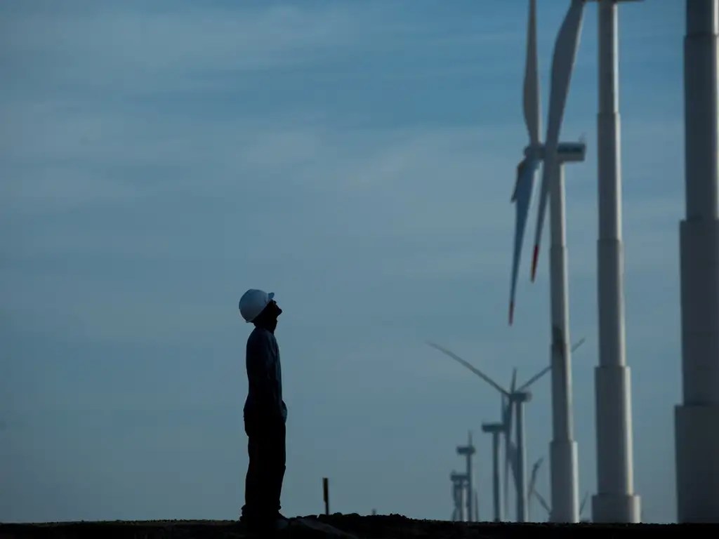 Foto de um engenheiro olhando para turbinas eólicas. A matéria trata de debêntures de infraestrutura