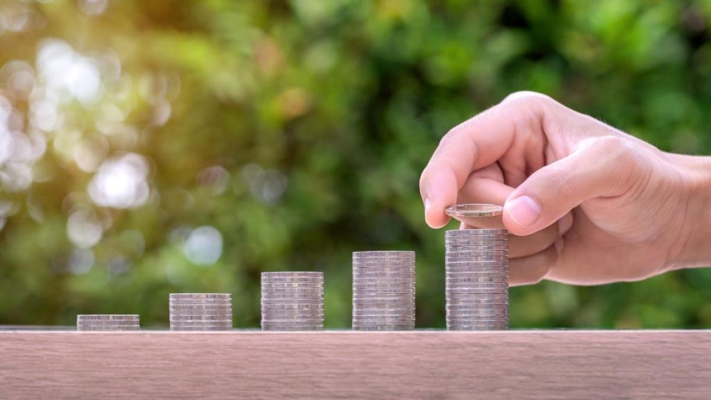 Foto para a matéria sobre quanto investir em fundos imobiliários para viver de renda em que aparece uma mão fazendo pilhas crescentes de moedas.