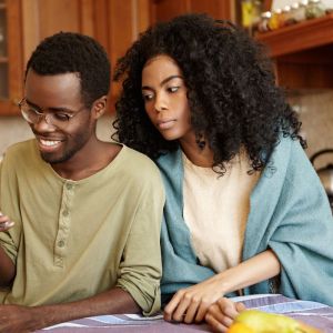 Imagem para matéria sobre conta internacional para menor de 18 anos em que aparece um rapaz negro olhando um celular sorrindo e ao seu lado uma mulher negra olhando para o celular também.