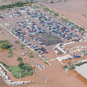 Foto de uma área afetada pelas enchentes no Rio Grande do Sul, mostra casas e instalações submersas. A matéria descreve o impacto do evento no PIB do Brasil.