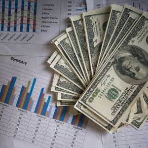 Imagem para a pauta sobre investimentos no exterior em que aparecem vários papeis com planilhas e por cima deles uma pilha de notas de 100 dólares.