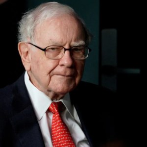 Foto de Warren Buffett, um homem branco, de óculos e cabelos brancos usando um terno preto com camisa branca e grava vermelha.