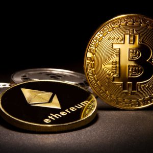 Foto de uma moeda de bitcoin, ou BTC, dourada ao lado de uma moeda de Ethereum, ou ETH, também dourada, sobre um fundo preto. A matéria explica se vale a pena investir em um ou outro.
