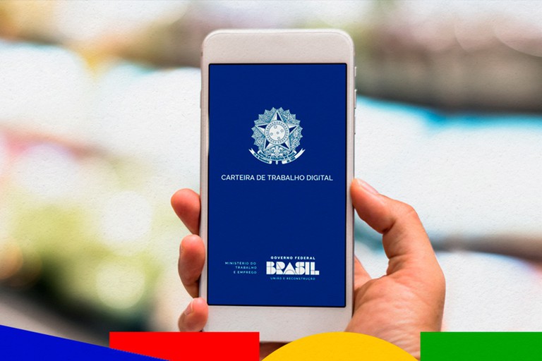 Foto de uma mão segurando um celular. Na tela, um fundo azul escrito "Carteira de trabalho digital".